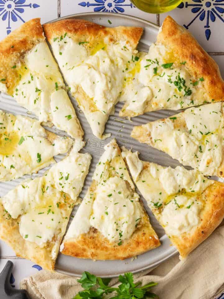 white pizza with ricotta cheese on a pizza pan cut into slices sprinkled with parsley.