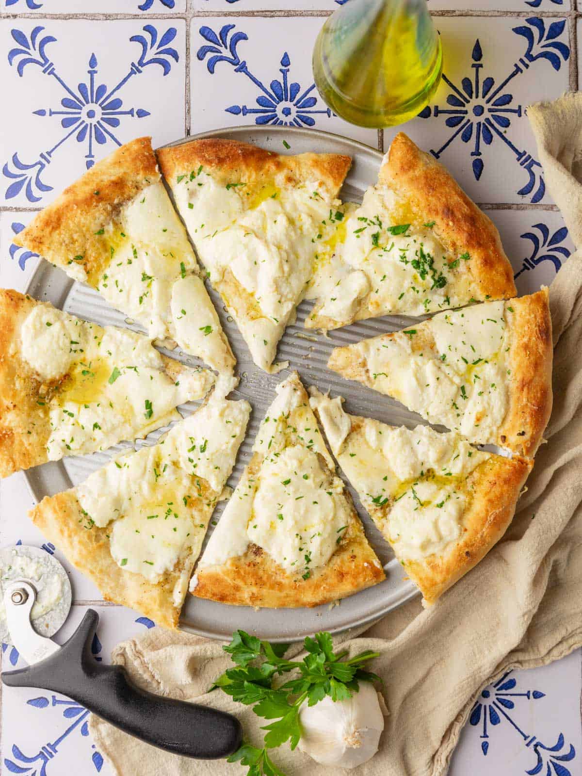 white pizza cut in slices with olive oil and garlic sauce, with melted cheese and chopped fresh parsley on top.
