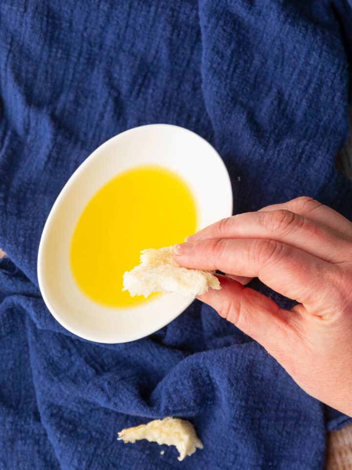 hand dipping a piece of bread into olive oil in a white dish.