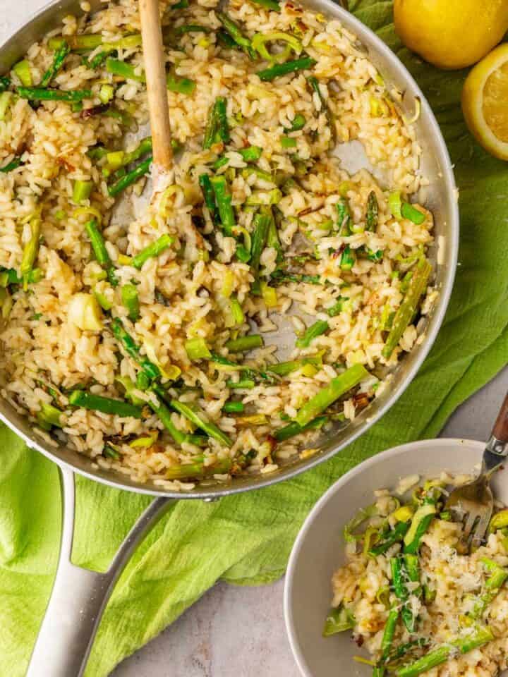 asparagus and leek risotto in a pan with a wooden spoon and bowl with a fork.