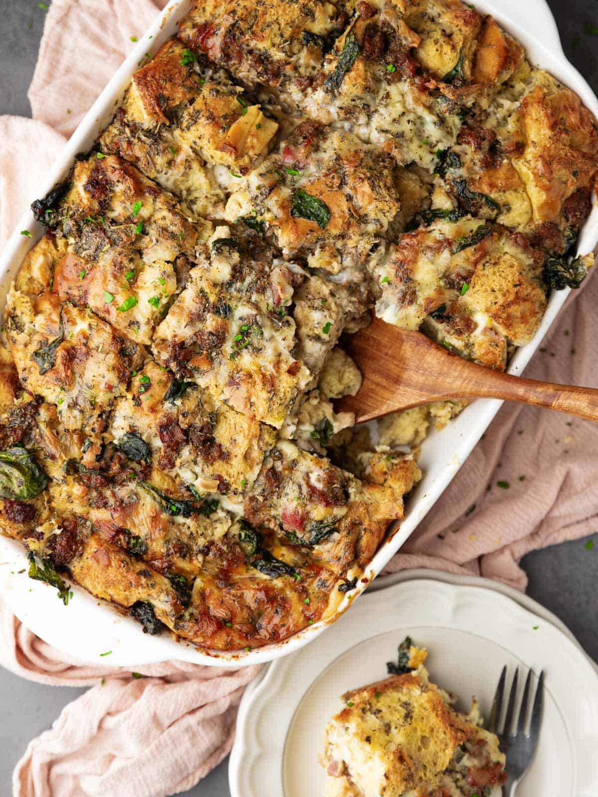 italian breakfast casserole in a white dish with a wooden spatula scooping out a serving.