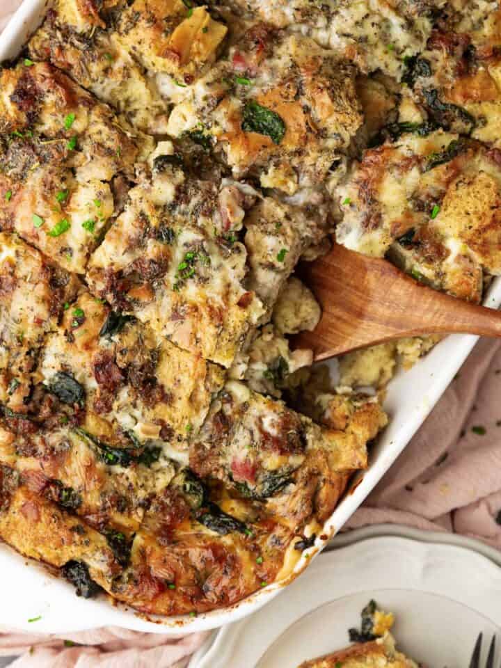 wooden spatula scooping a serving of Italian breakfast strata with sausage, spinach, pancetta and fo