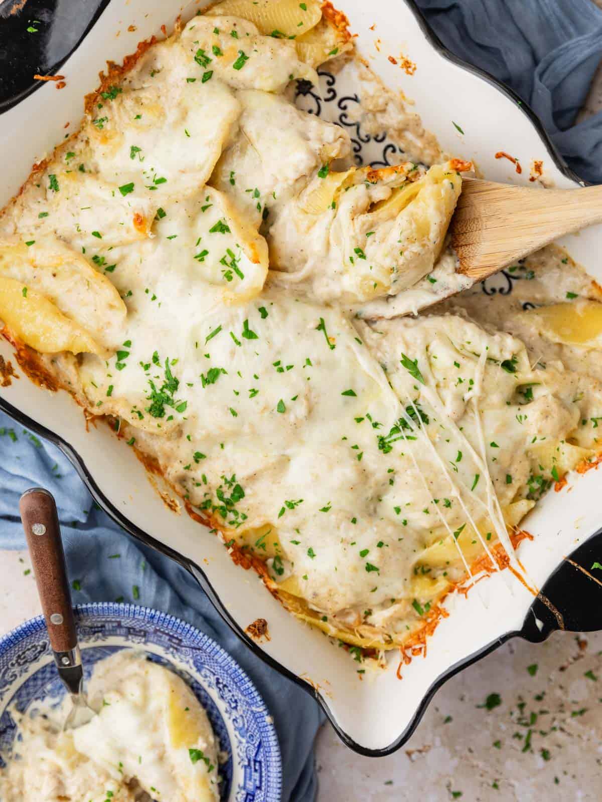 wooden spoon scooping stuffed shells with alfredo out of a pan.