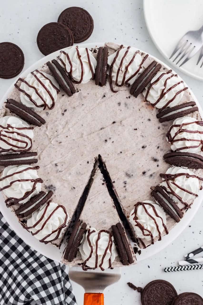 oreo cheesecake topped with whipped cream and oreos with one slice cut from it.