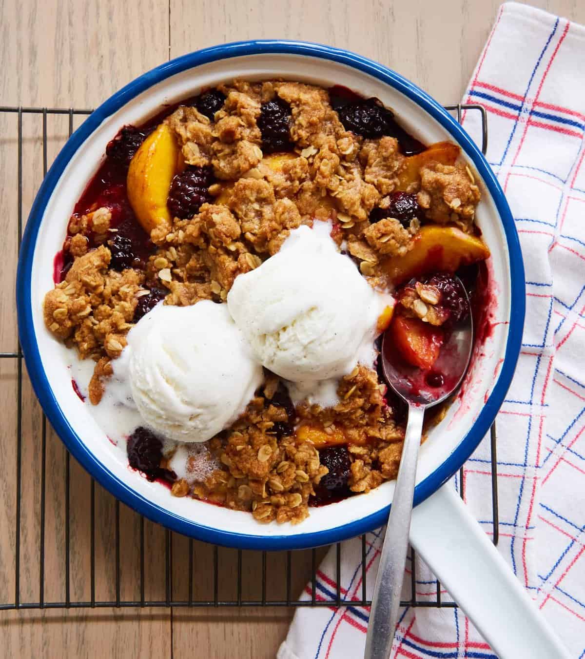 peach and blackberry crisp in a pan topped with vanilla ice cream.