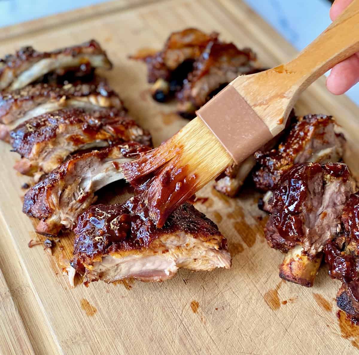 brush spread bbq sauce on cut ribs on a cutting board.