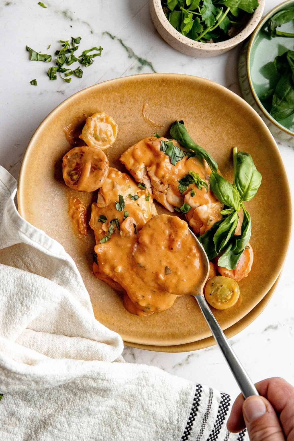 creamy tomato chicken on a plate with a spoon pouring sauce on it.