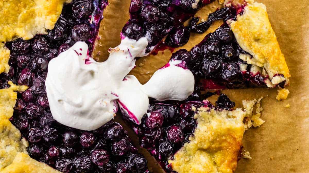 blueberry crostata topped with fresh whipped cream with a few slices cut from it.