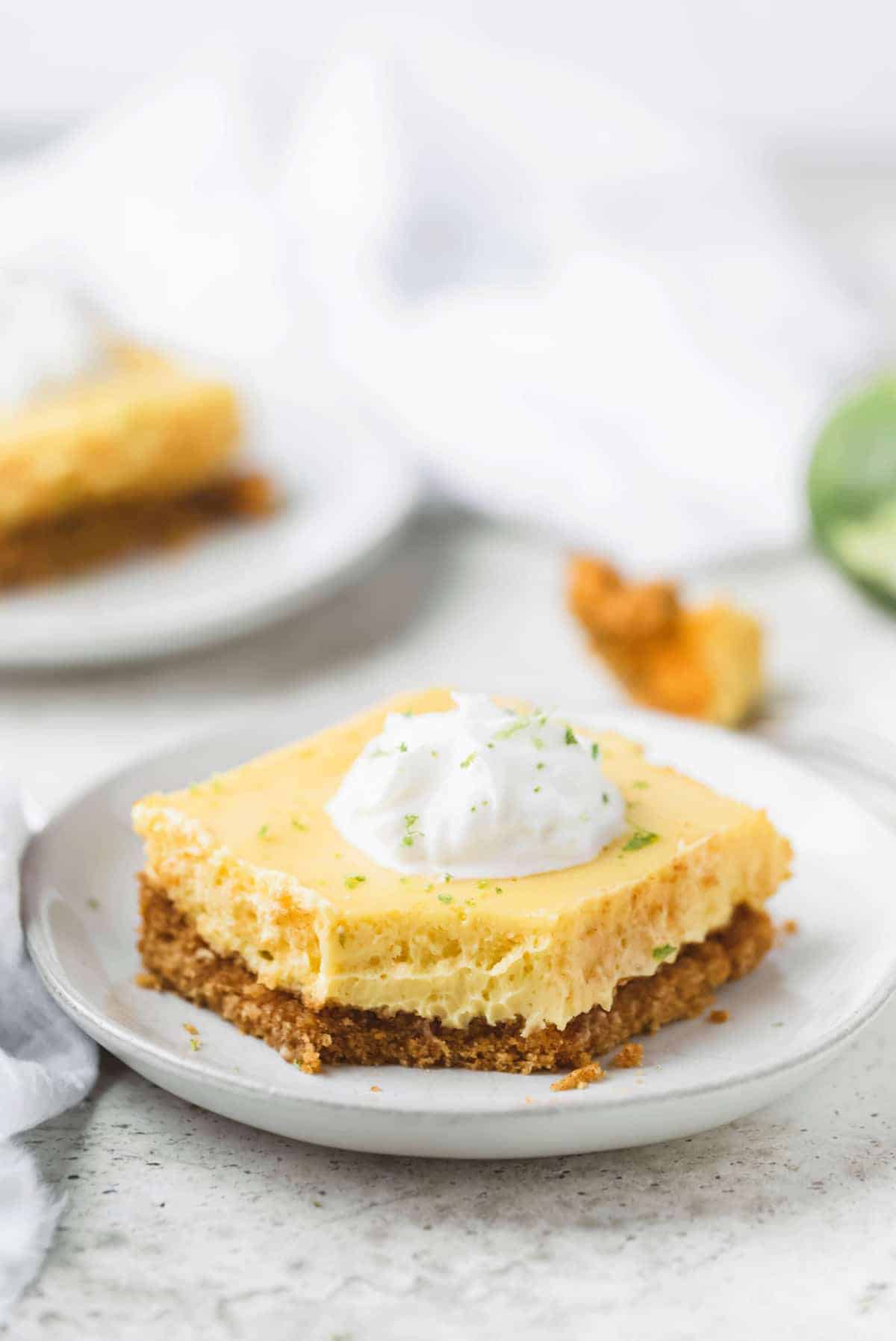 key lime pie bar on a plate with whipped cream and a bite taken from it.