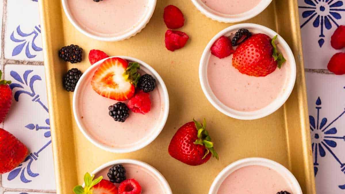 strawberry panna cotta in white ramekins topped with fresh berries.