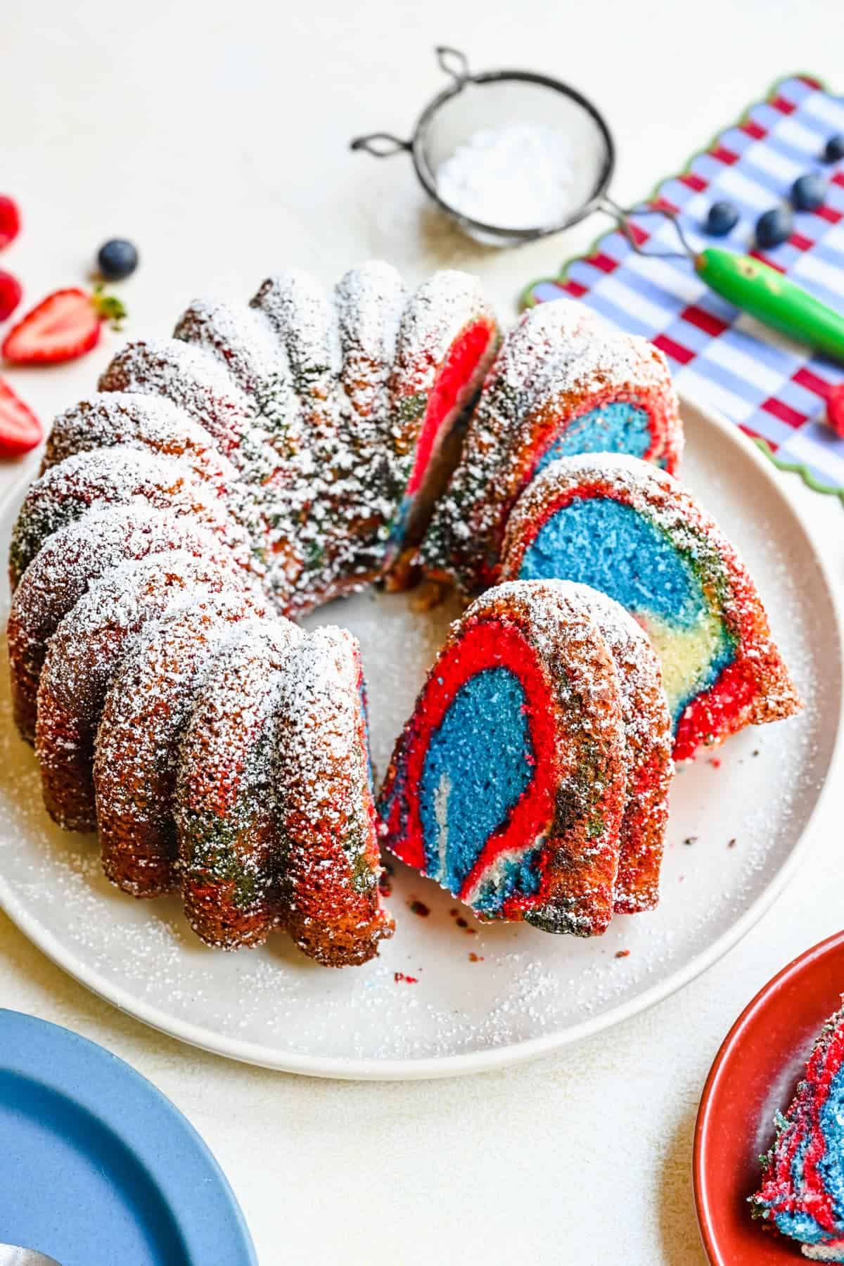 partially sliced bundt cake with red, white and blue swirls inside, sprinkled with powdered sugar on top.