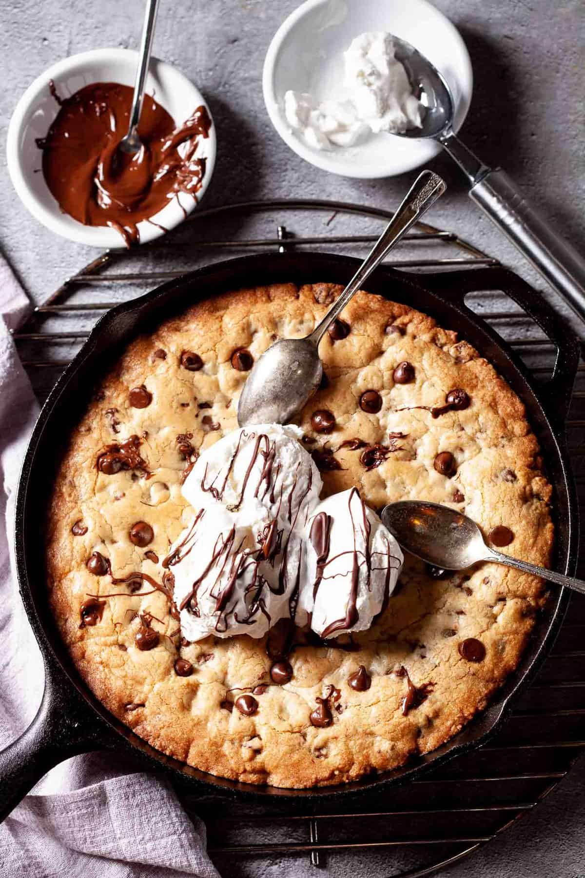 skillet chocolate chip cookie topped with three scoops of ice cream and drizzled with chocolate syrup.