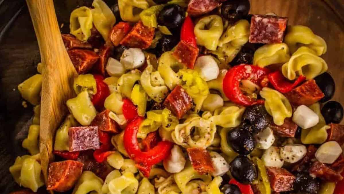 antipasto style pasta salad in a bowl with wooden spoon.