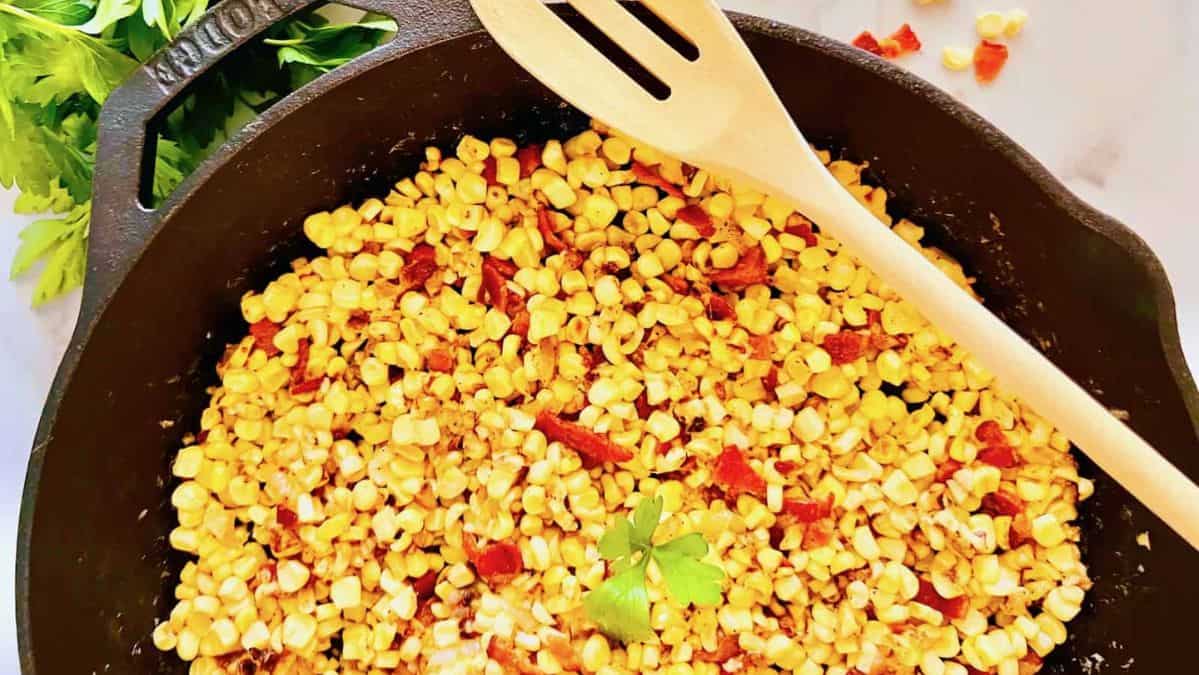 corn with bacon in a cast iron skillet with a wooden spoon.