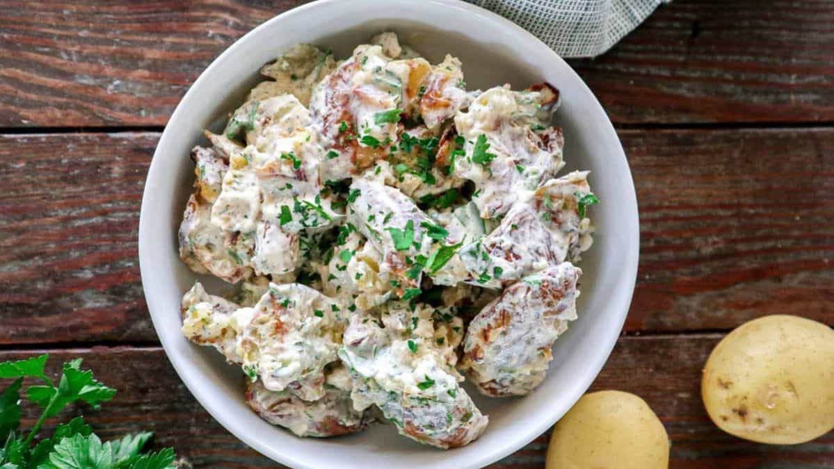 white bowl filled with potato salad with parsley on top.