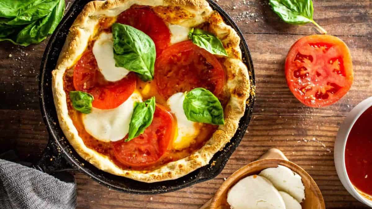 cast iron skillet pizza with mozzarella, tomatoes and fresh basil.