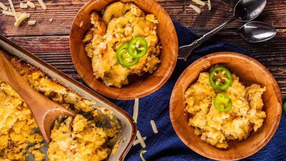 cornbread cassrole in a pan with two servings in bowls topped with fresh jalapeno slices.