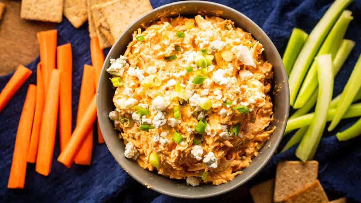 buffalo chicken dip in a bowl topped with crumbled blue cheese and scallions.