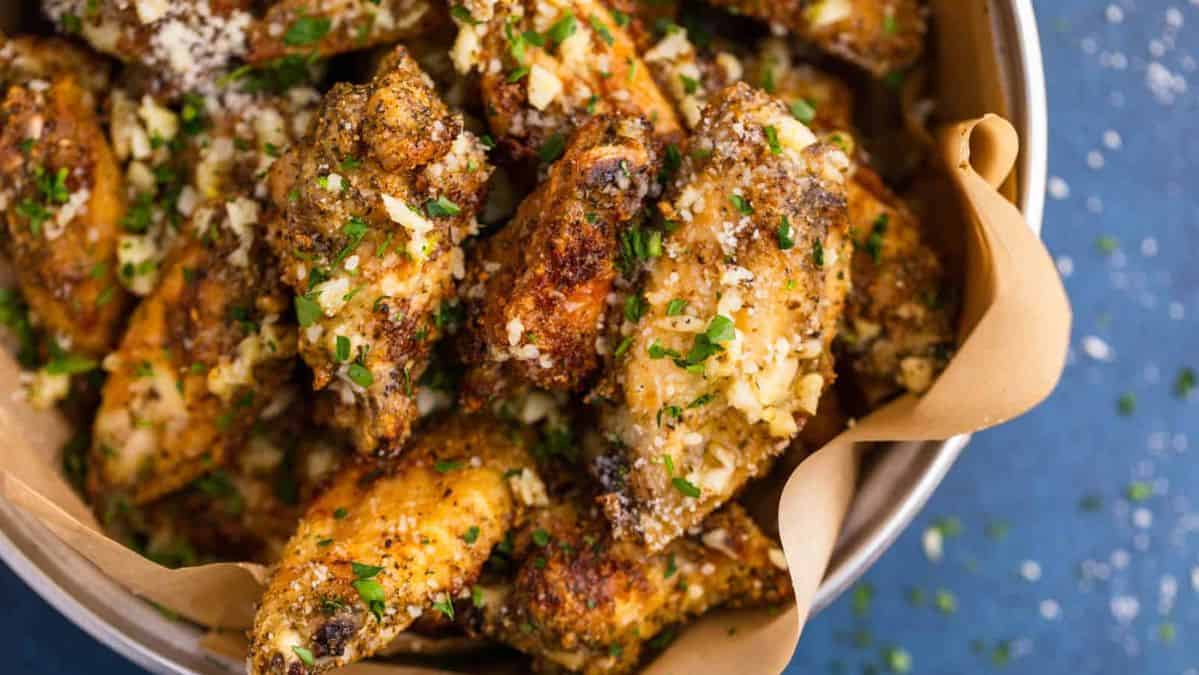 Garlic Parmesan chicken wings in a dish over parchment paper with Parmesan cheese and herb sprinkled on top.