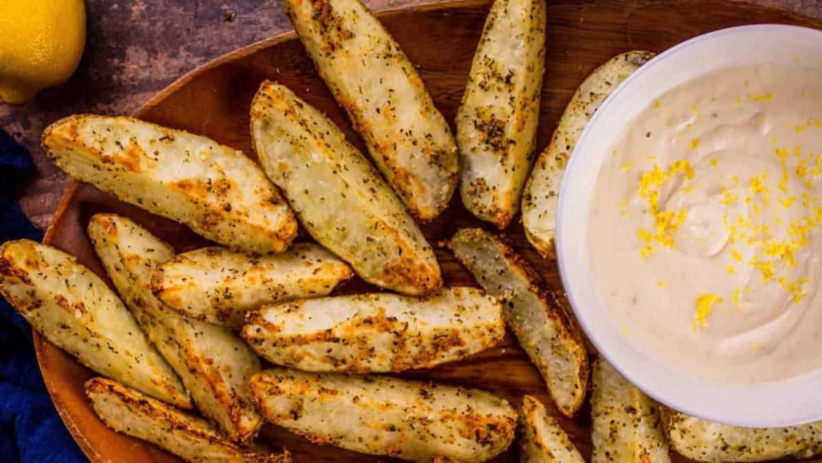 crispy potato wedges on a platter next to a white bowl of lemon aioli.