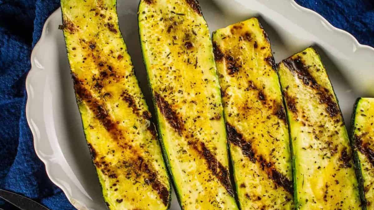 grilled zucchini halves on a white platter.