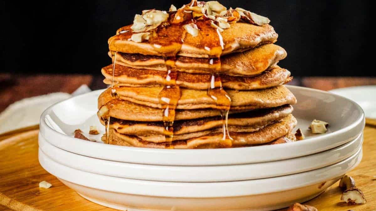 stack of nutella flavored pancakes on a stack of plates topped with syrup and crushed hazelnuts.