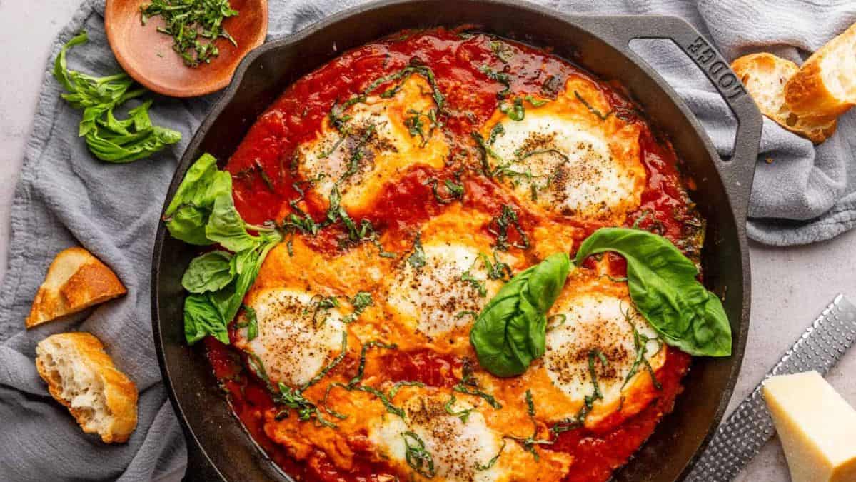 poached eggs in a tomato sauce in a cast iron skillet garnished with fresh basil leaves.