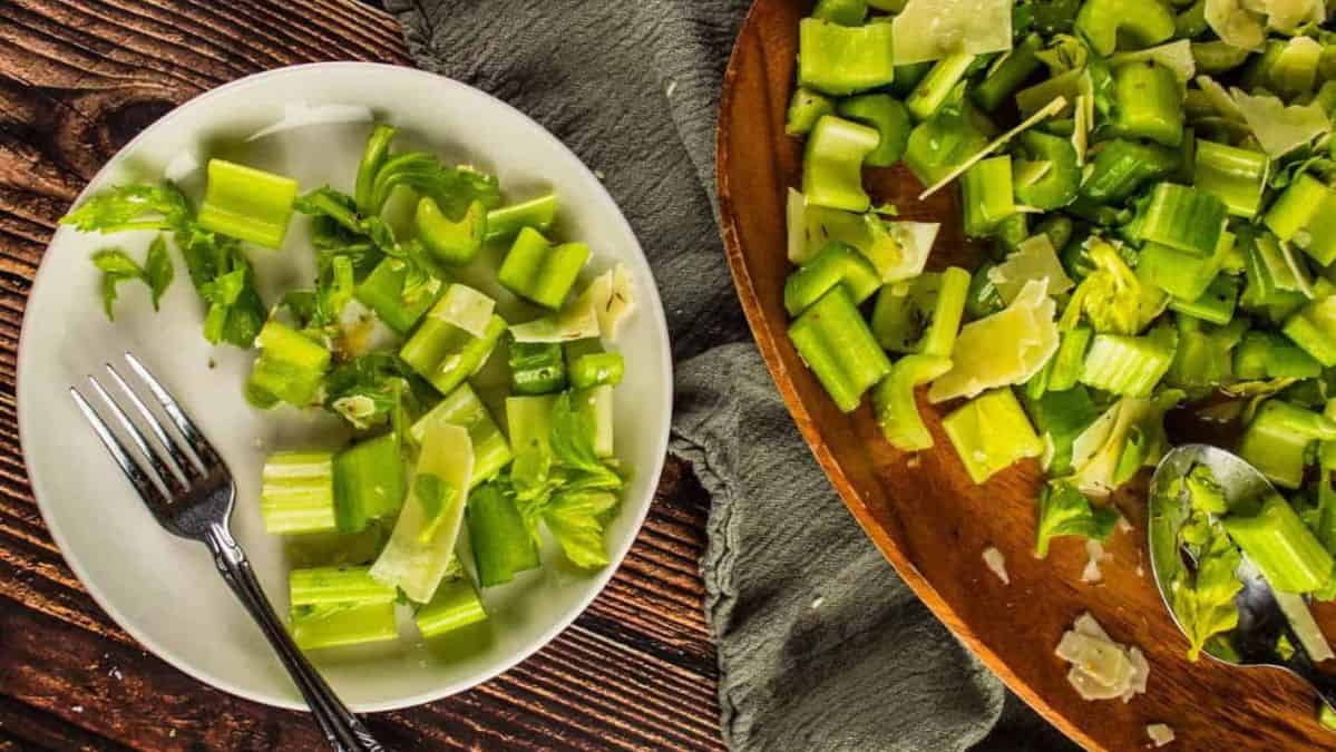 celery salad with parmesan cheese on a wooden platter and on a white plate with a fork.