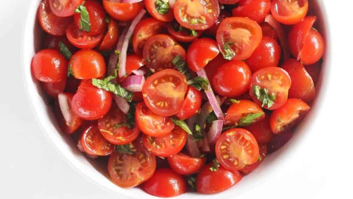 tomato salad with fresh basil and red onion in a white bowl.