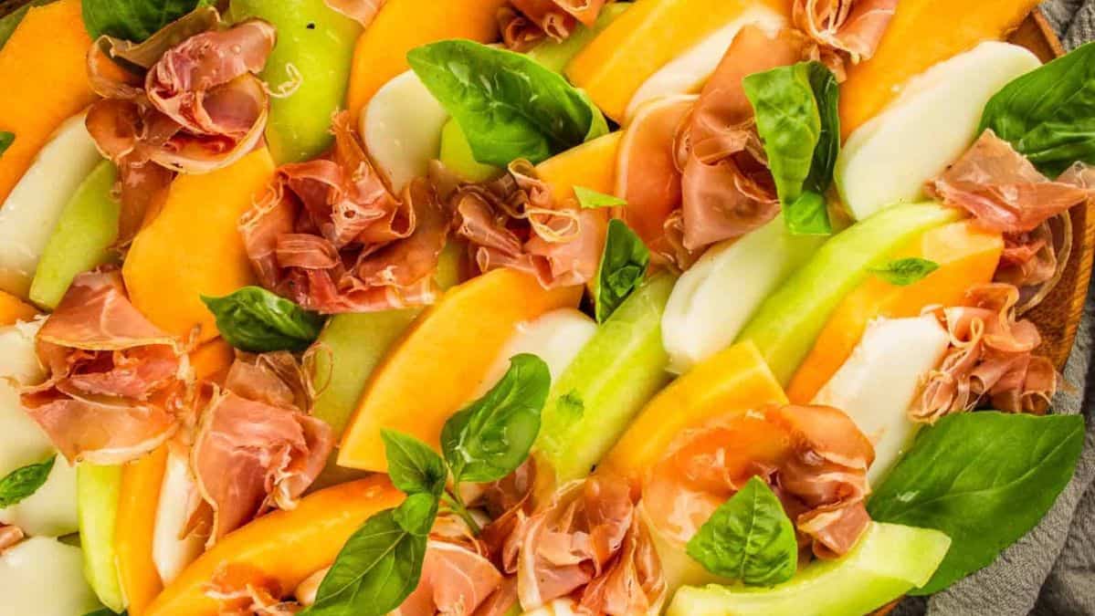 close up shot of sliced honeydew and cantaloupe layered with prosciutto, fresh mozzarella and basil.