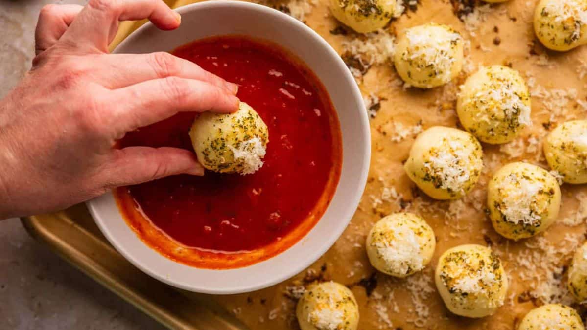 hand dipping a herb and cheese coated bread bite into marinara.