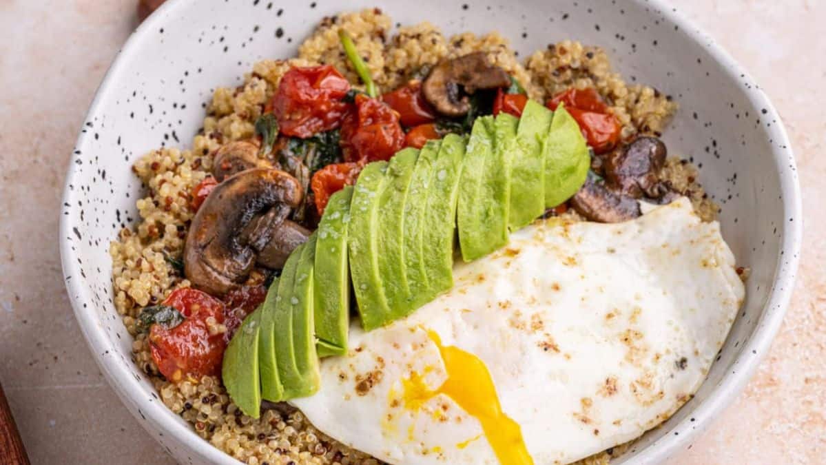 quinoa and veggies in a bowl topped with sliced avocado and eggs.