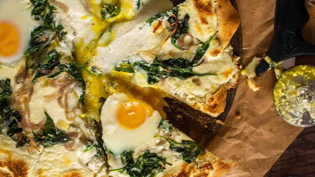 sliced breakfast pizza topped with ricotta, eggs, spinach and red onion.