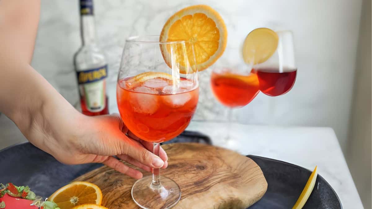 hand holding a wine glass with an aperol spritz garnished with a  orange slice.