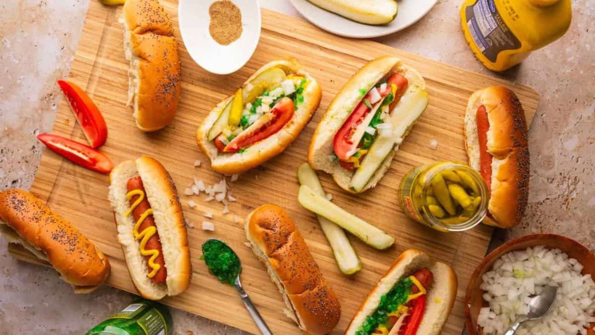 chicago style hot dogs on a cutting board with toppings around.