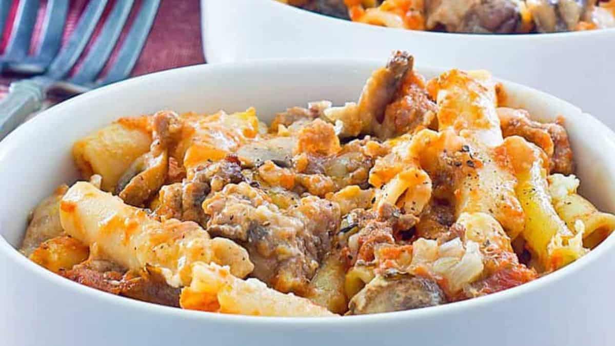 white bowl of cheesy baked ziti pasta with sausage.