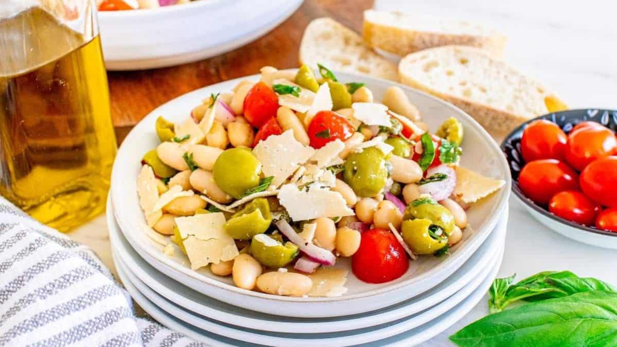 stack of white bowls with the top one filled with a bean salad with tomatoes, olives and cheese.