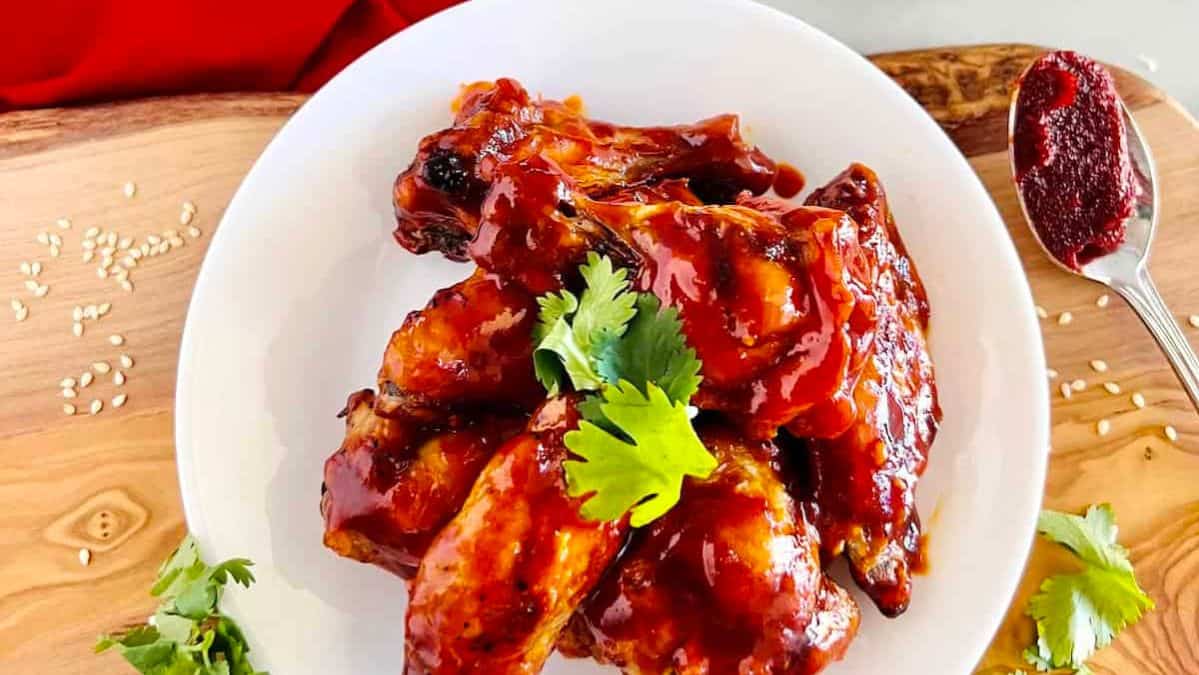 wings with a dark red sauce on a white plate topped with fresh cilantro.