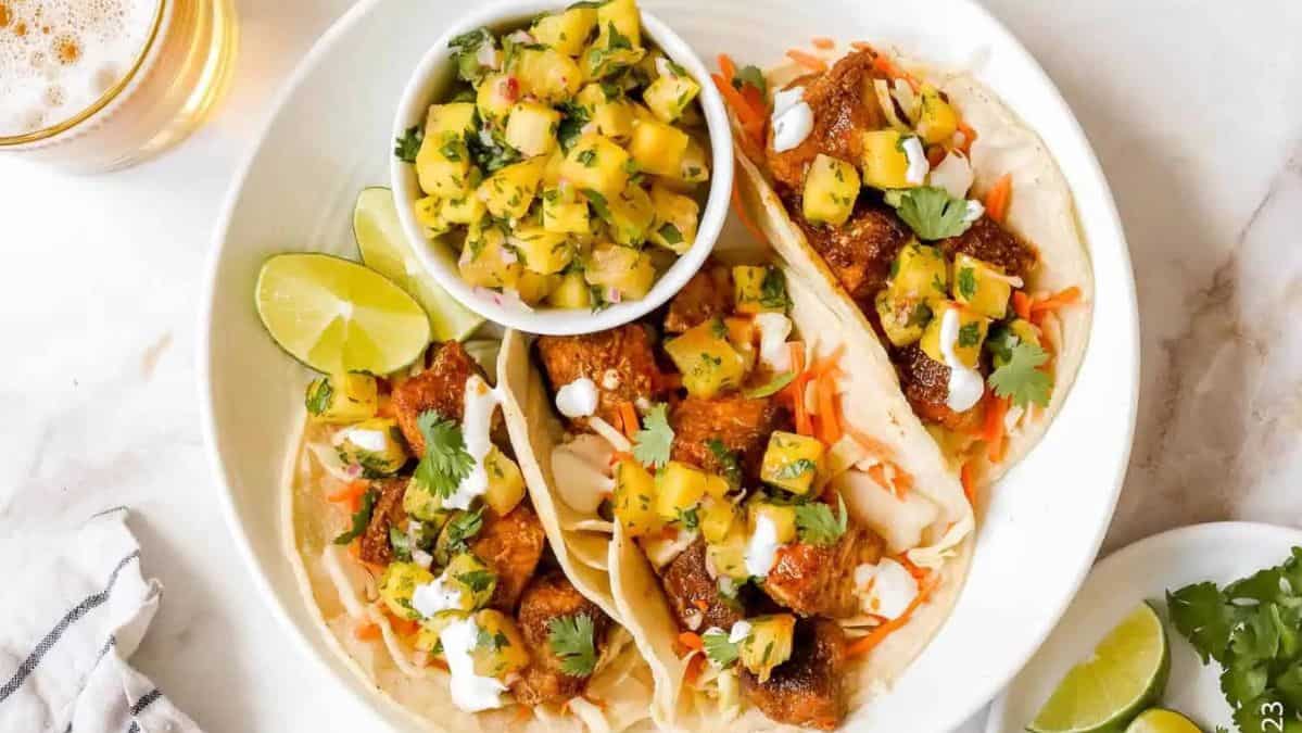 three tacos on a plate with meat, cheese and pineapple salsa.