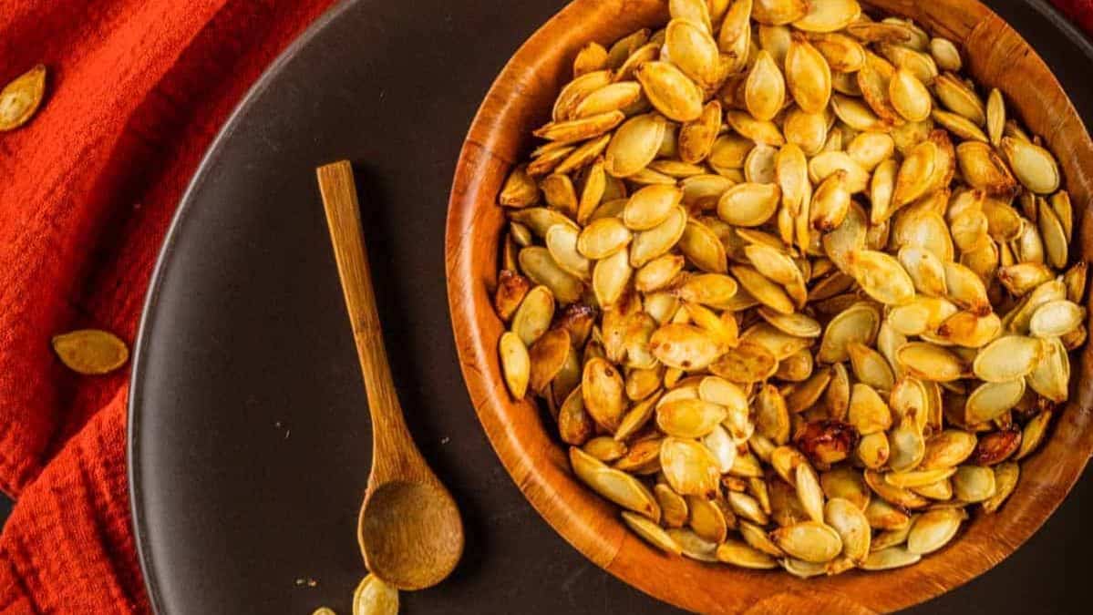 roasted pumpkin seeds in a bowl with a small wooden spoon next to it.