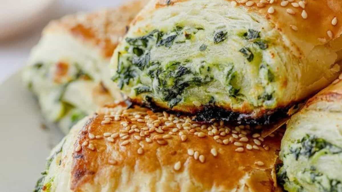 spinach and cheese puff pastry rolls topped with sesame seeds, stacked on top of each other.