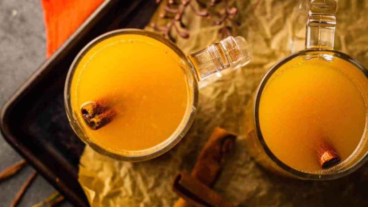 Overhead view of two clear glass mugs with apple cider cocktail with cinnamon sticks floating in them.