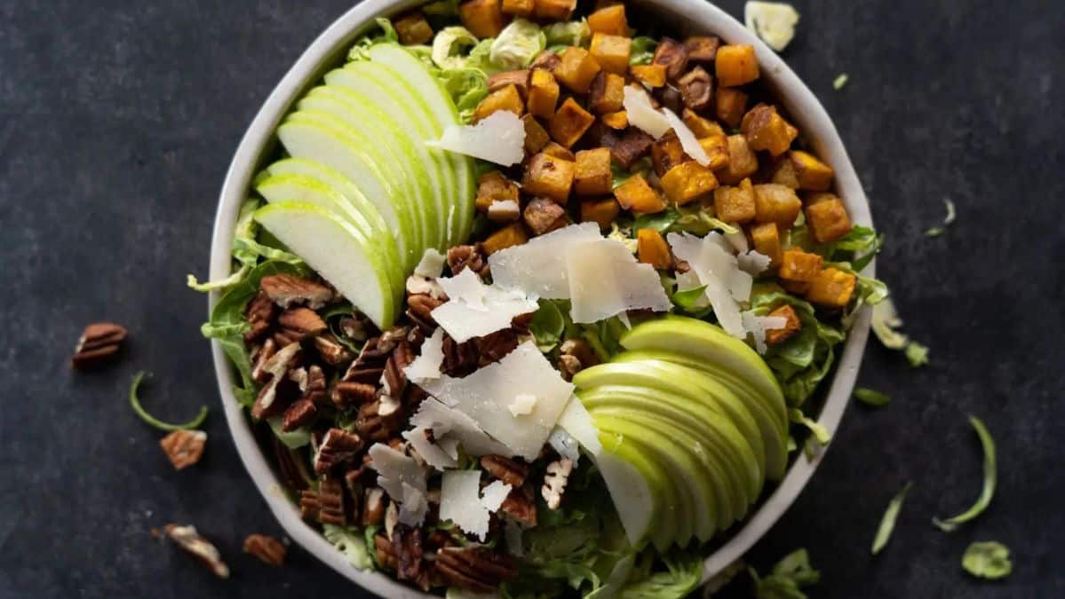 Brussels sprout salad topped with cheese, sweet potatoes, nuts and sliced apples.