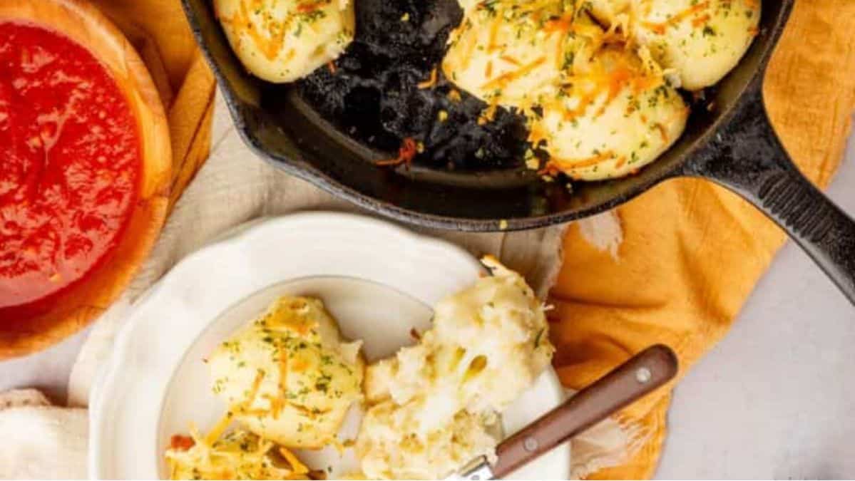 Round pieces of bread in a cast-iron skillet with a couple pulled open to see the cheese inside on a white plate with a fork next to it.