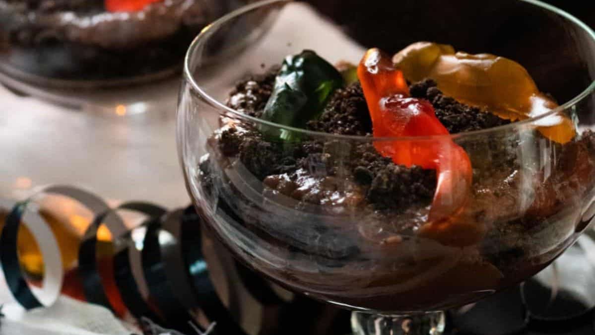 Chocolate pudding in a cup topped with crushed chocolate cookies and gummy worms.