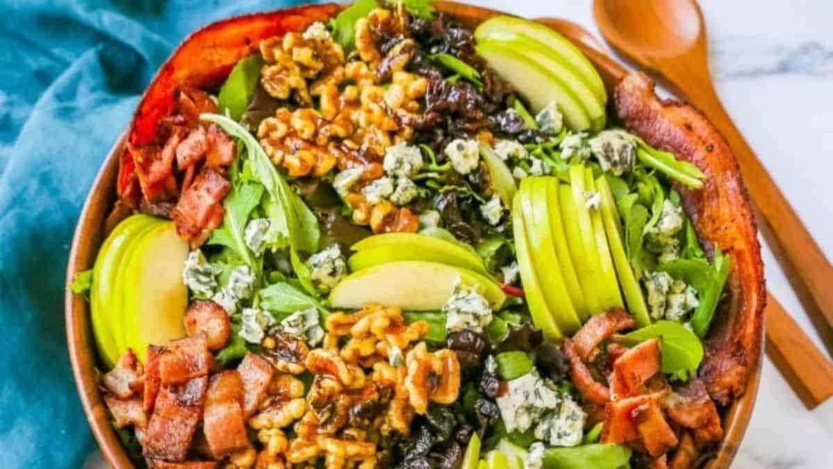 Salad topped with walnuts, sliced apples, cheese, and dried fruit.