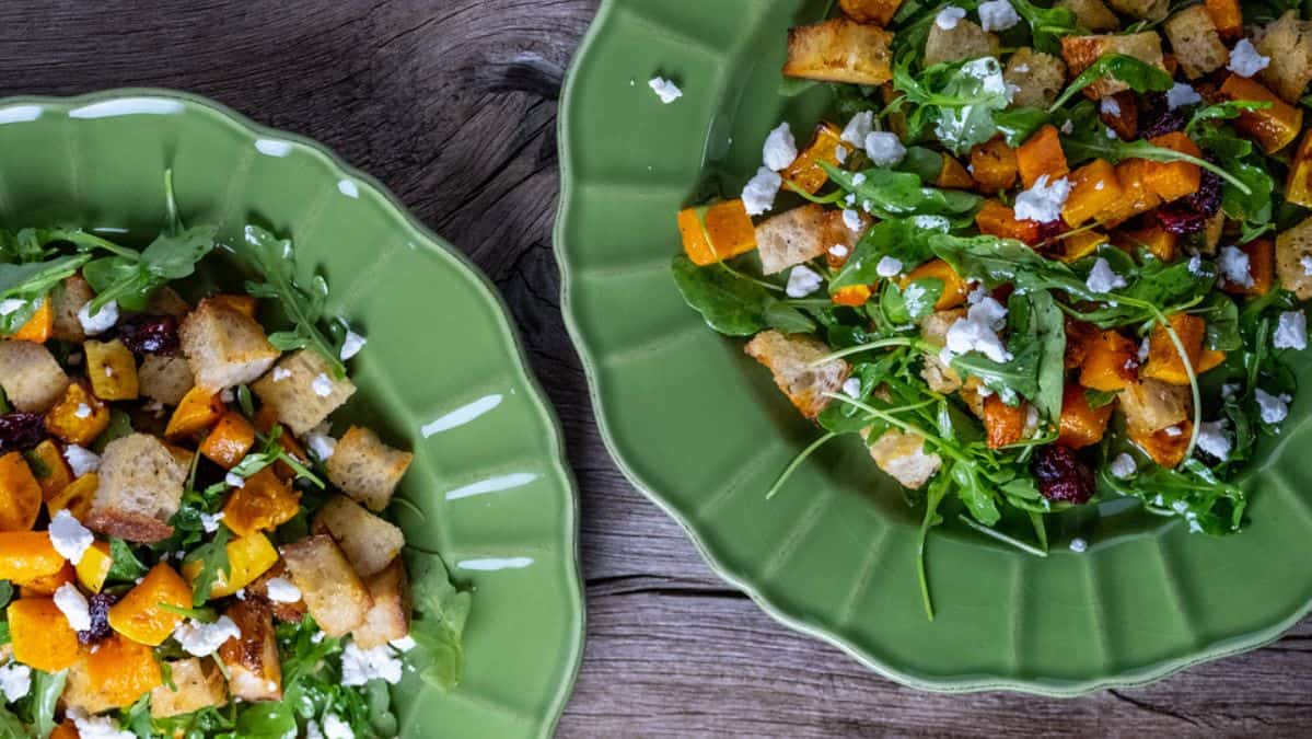 Two salads on green plates topped with cheese and bread.