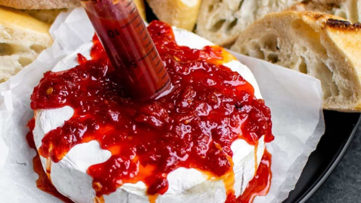 A wheel of breeze on a plate topped with cranberry sauce with a knife sticking into it.