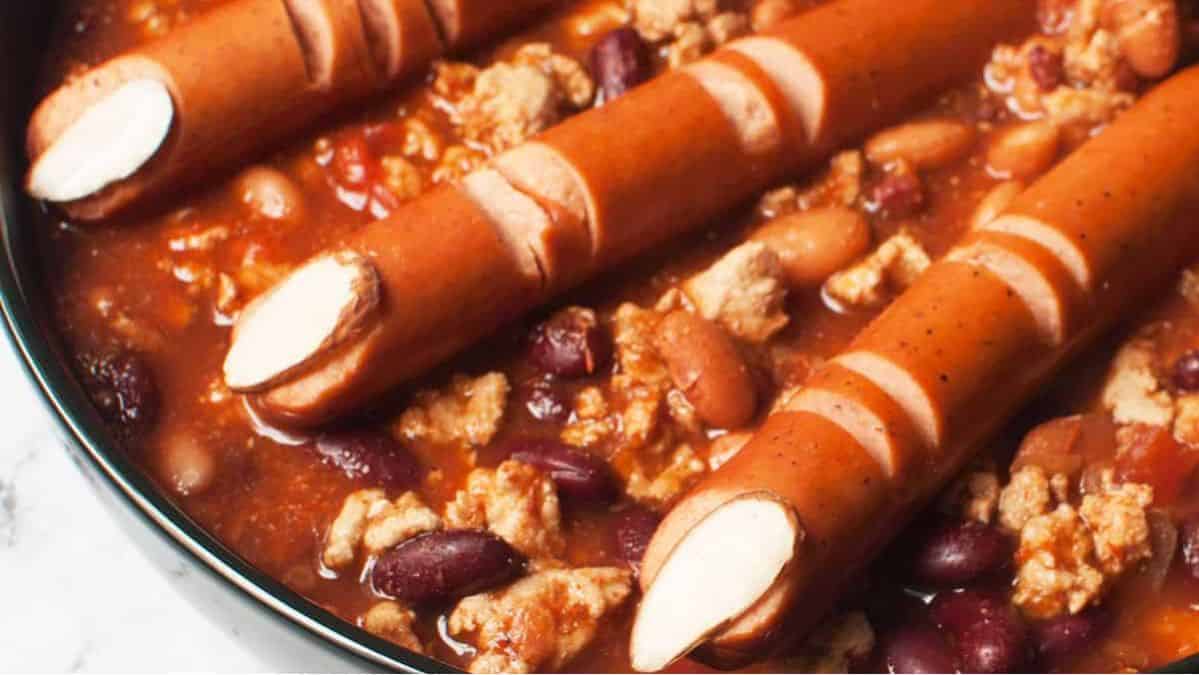 Chili in a pot topped with hotdogs made look like fingers.