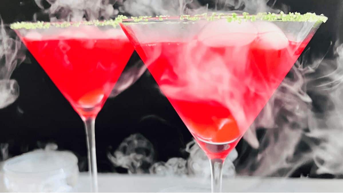 Two martini classes filled with a red cocktail with dry ice smoke around.